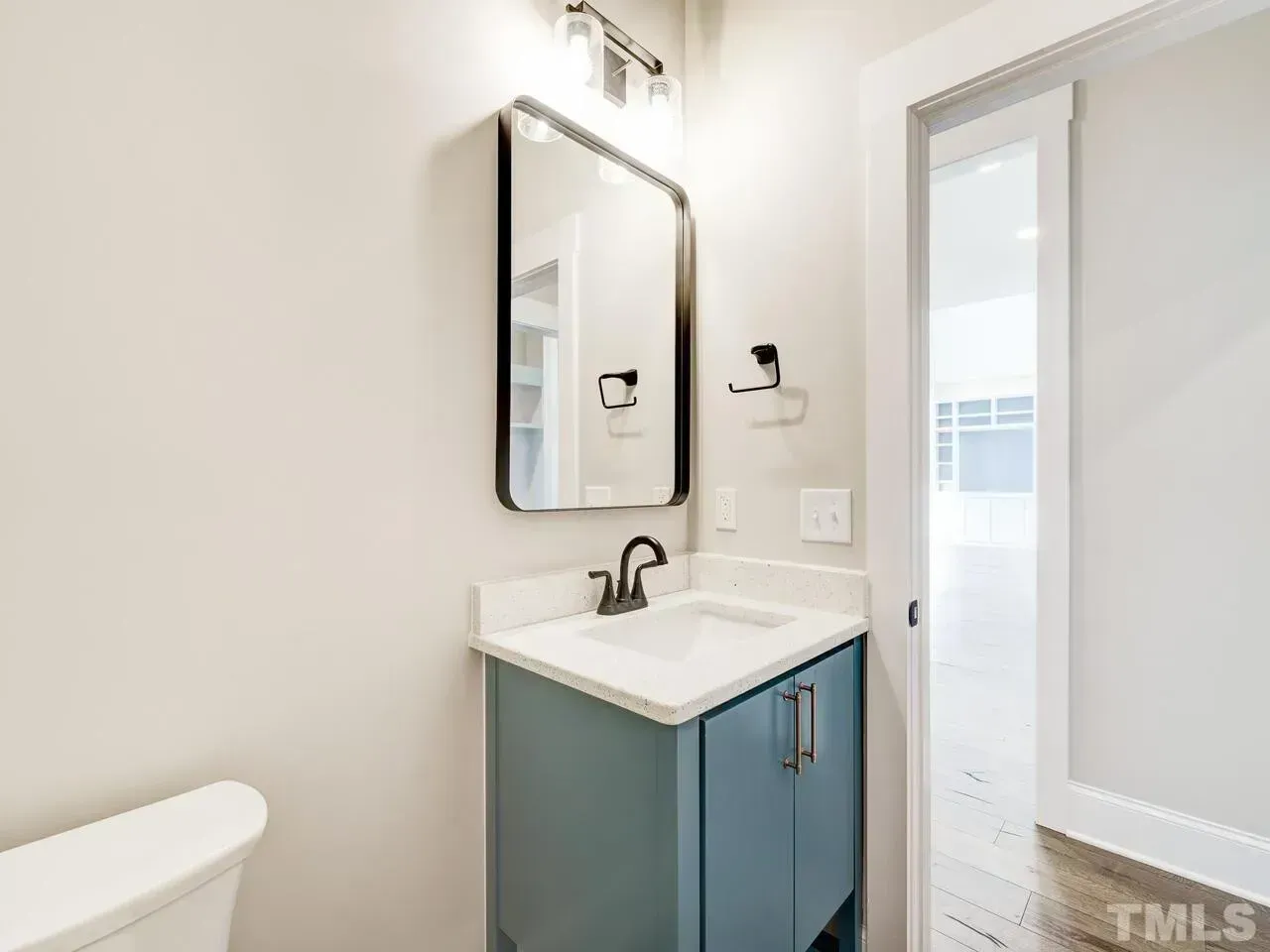 A small bathroom with a blue vanity, white countertop, silver faucet, rectangular mirror, and a partial view of a toilet.