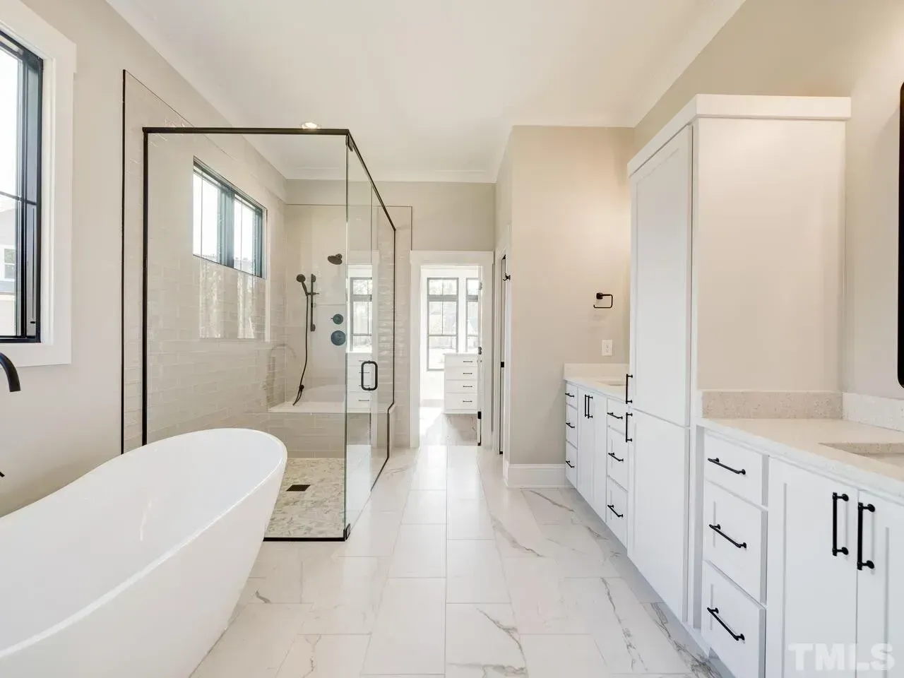 A modern bathroom featuring a white soaking tub, a large glass-enclosed walk-in shower, and white cabinets on marble floors.