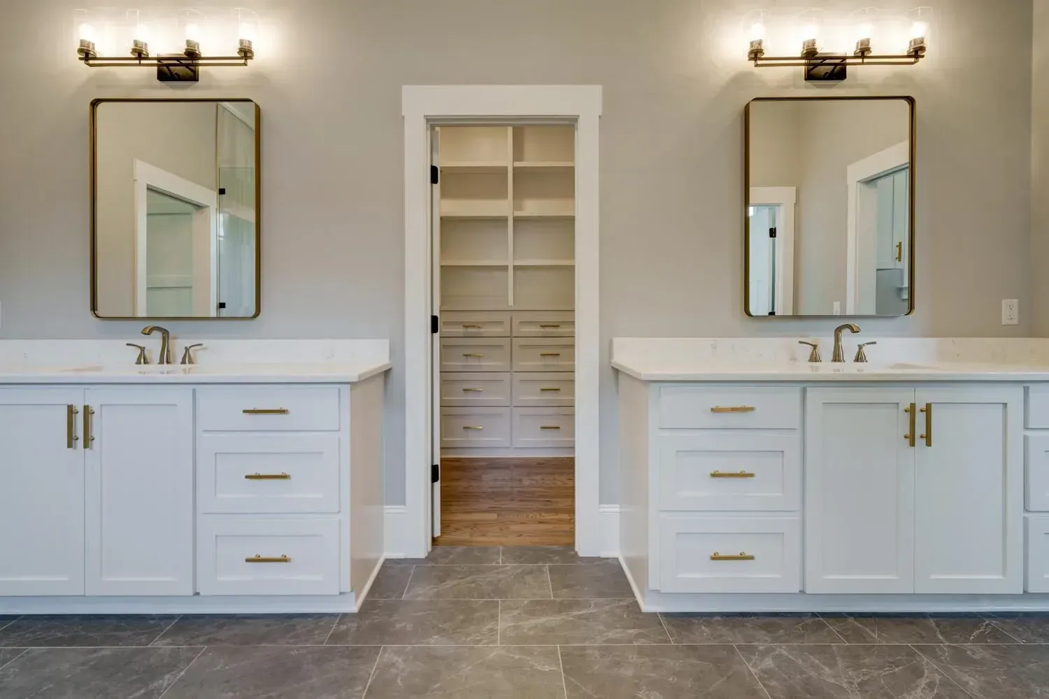 Double vanity with white cabinets, gold hardware, rectangular mirrors, and lighting, flanking a walk-in closet.