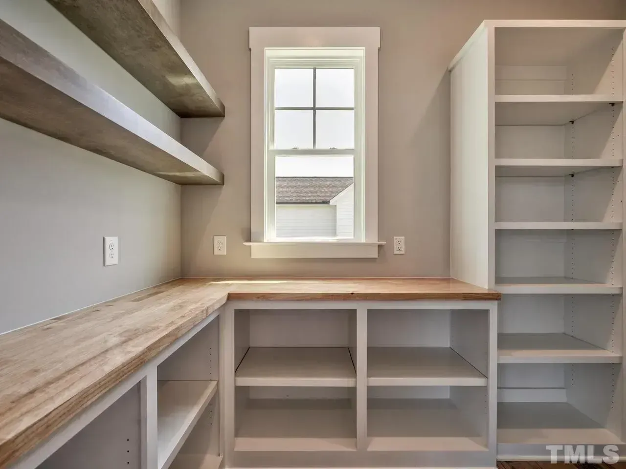 A light-colored pantry or laundry room with a window, wooden countertops, open lower shelving, and floor-to-ceiling unit.