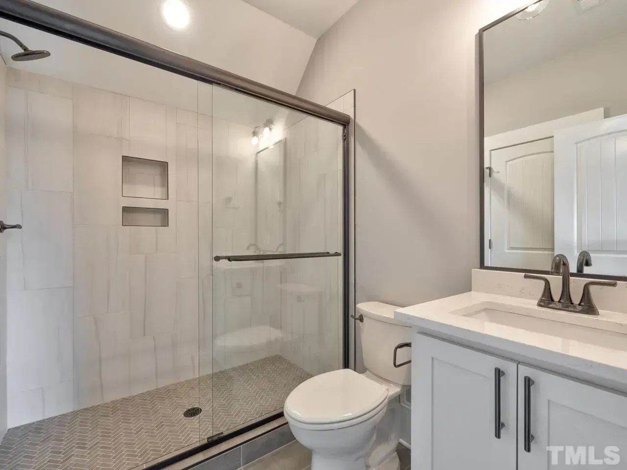 A modern bathroom featuring a glass-enclosed walk-in shower with tiled walls, a white toilet, and a vanity with a mirror.