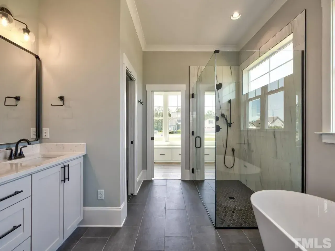 A modern bathroom featuring a white vanity with black hardware, a tiled walk-in glass shower, and a soaking tub.