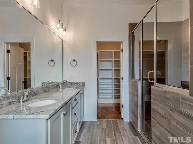 A modern bathroom featuring a grey vanity with a marble countertop, a large mirror, and a glass-enclosed walk-in shower.