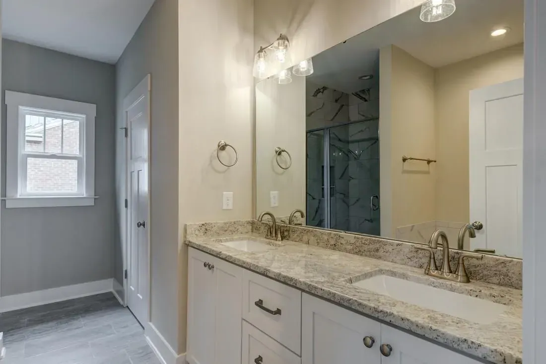 Modern bathroom with a double vanity, speckled granite countertop, white cabinets, and a wall-to-wall mirror.