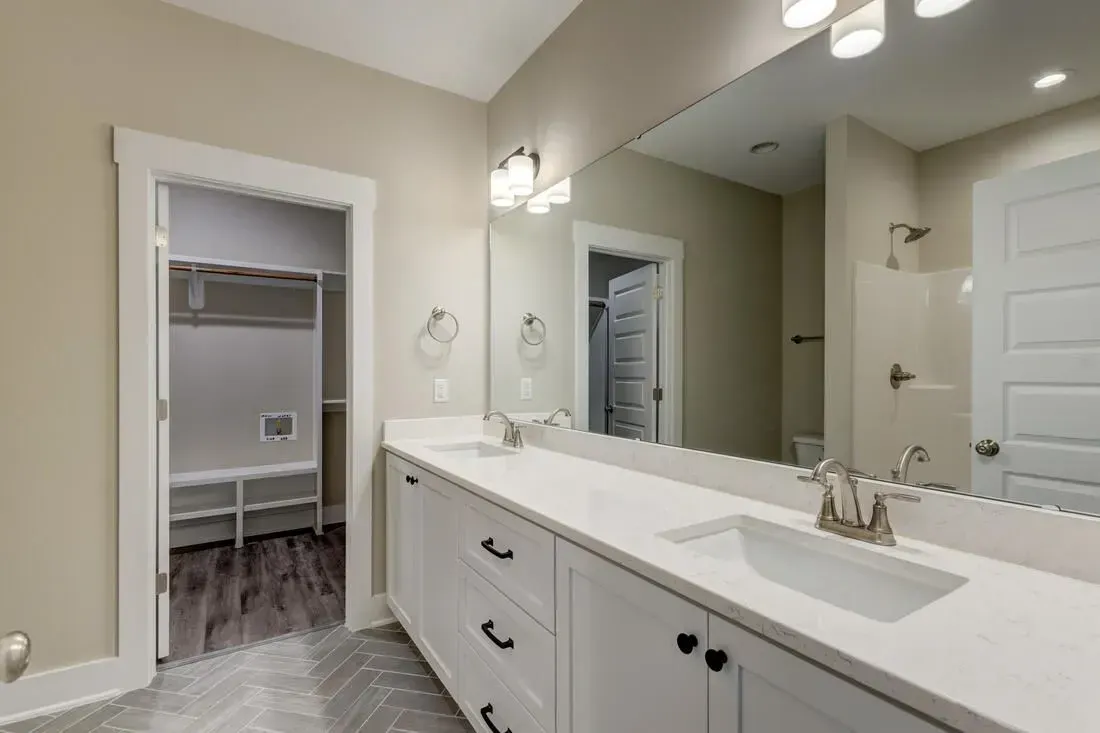 A modern bathroom with a white vanity, quartz countertop, large mirror, and an open doorway leading to a walk-in closet.