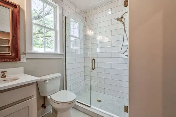 A bathroom featuring a white toilet, a vanity with a white countertop, and a walk-in shower with white subway tiles.