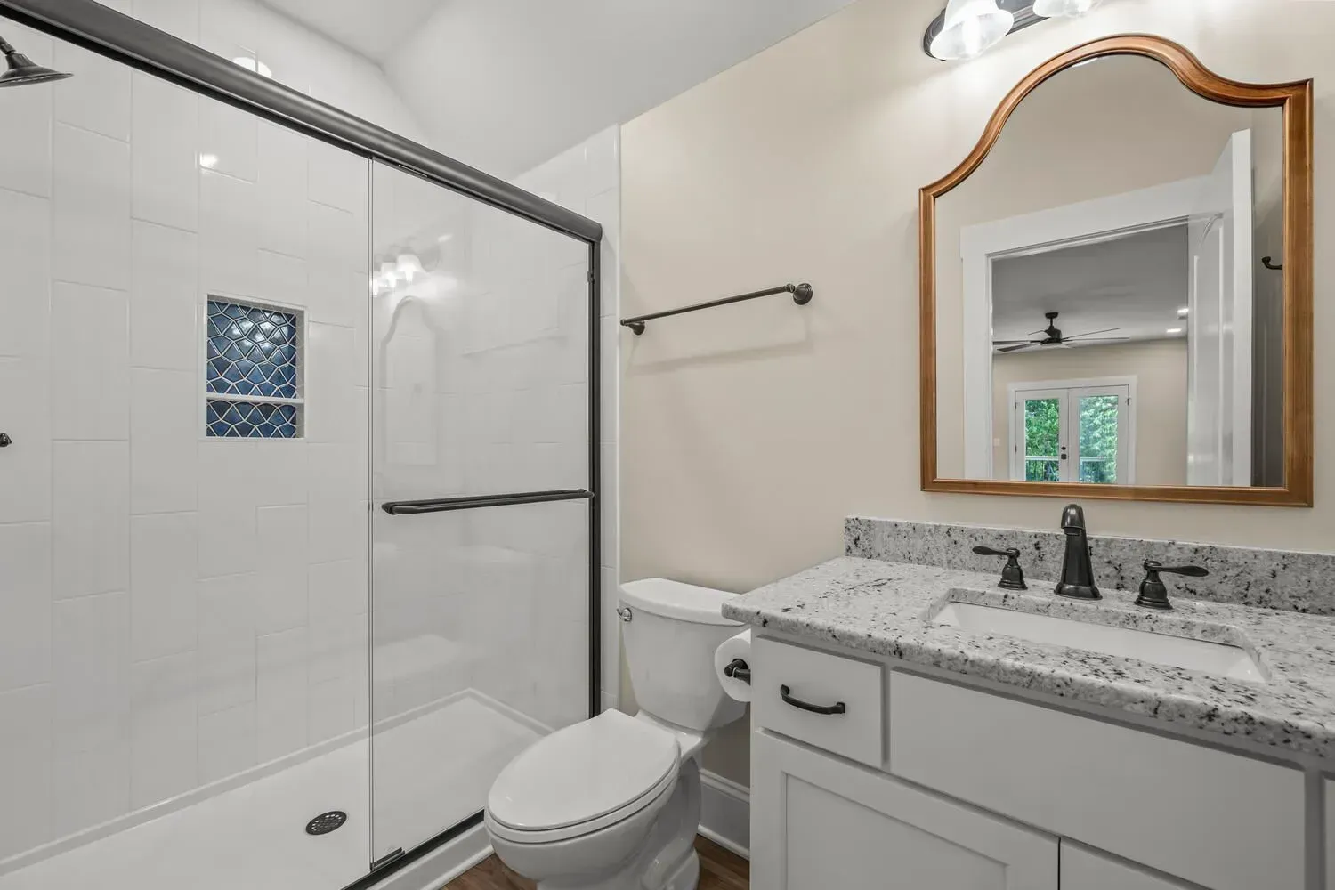 A modern bathroom with a glass-enclosed shower, a white vanity with granite countertops, and an arched wall mirror.