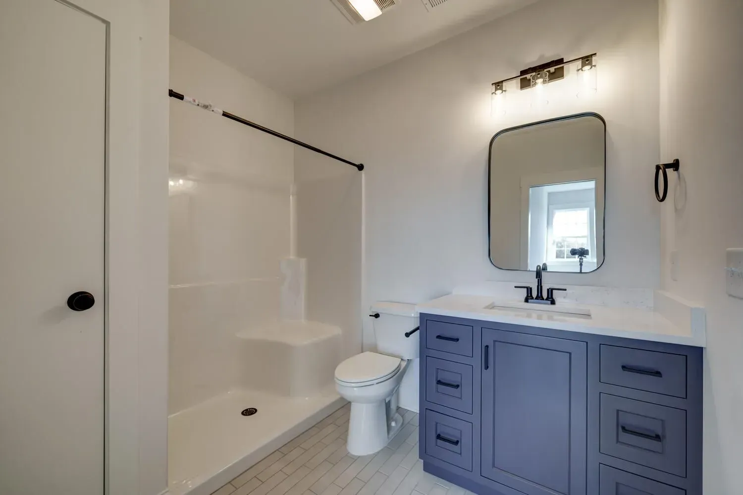 Modern bathroom with white walls, a walk-in shower, a white toilet, and a navy blue vanity with a framed mirror.