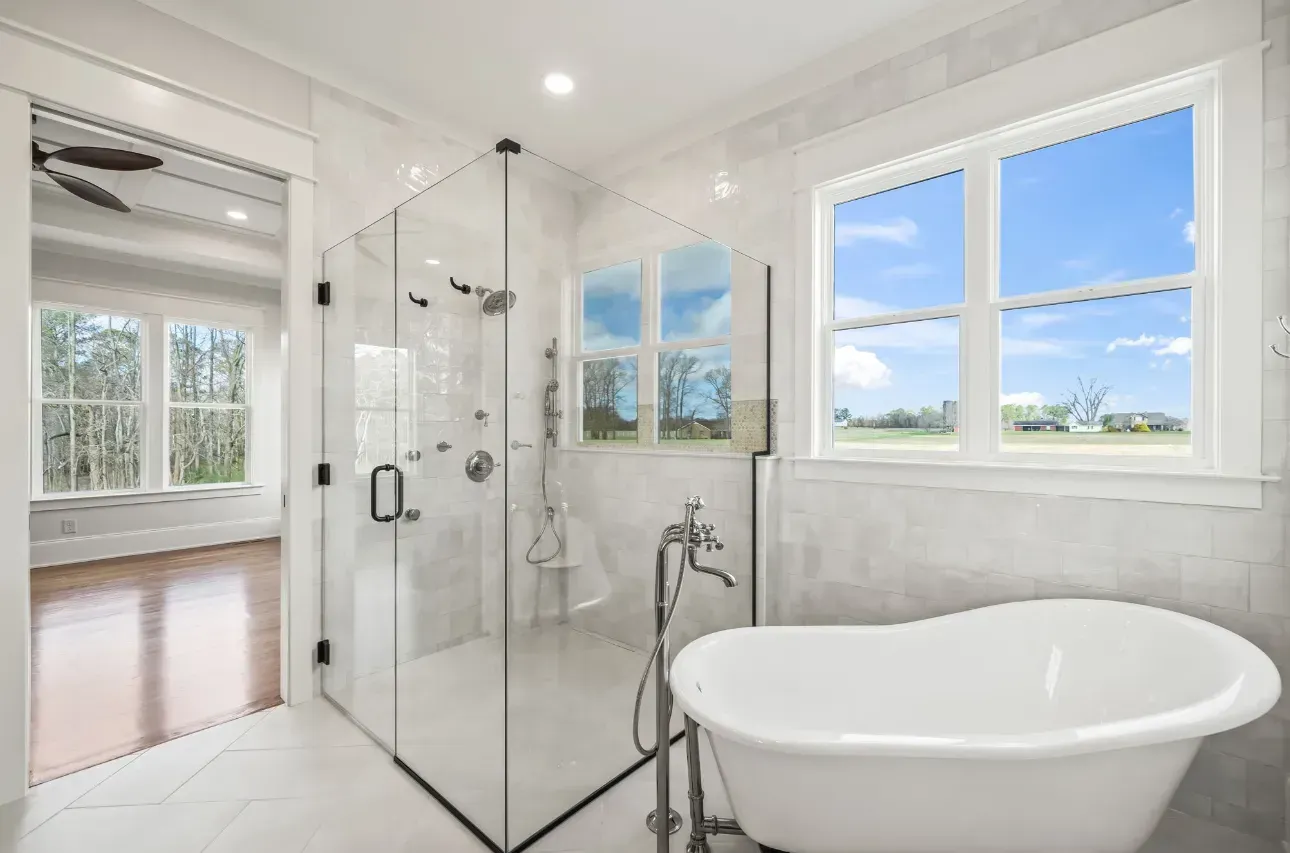 A bright, modern bathroom featuring a white freestanding soaking tub, a large glass-enclosed shower, and wide windows.