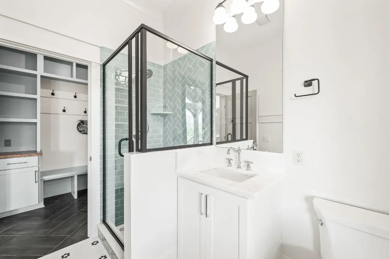 A modern bathroom with a glass-enclosed shower, a white vanity with silver fixtures, and a walk-in closet in the background.
