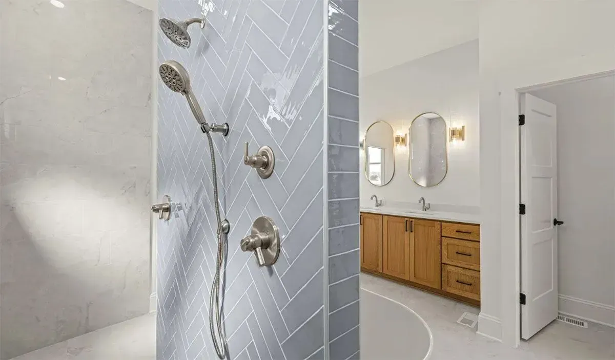 Modern bathroom with a herringbone-tiled shower, brushed nickel fixtures, and a wooden double vanity with oval mirrors.