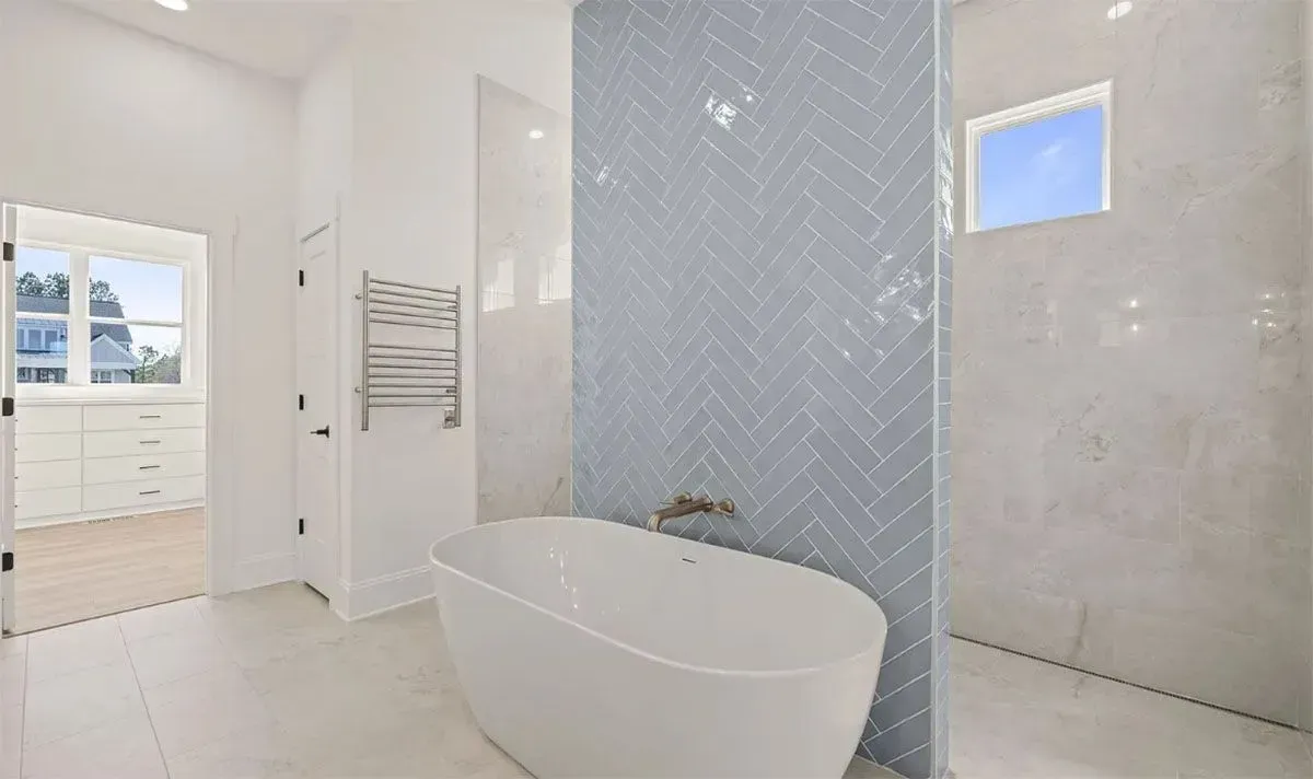 A modern bathroom featuring a white freestanding tub in front of a blue herringbone-tiled accent wall and a walk-in shower.