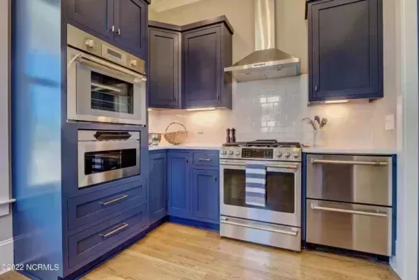 A kitchen with navy blue cabinets, stainless steel appliances, a range hood, and light-colored countertops.