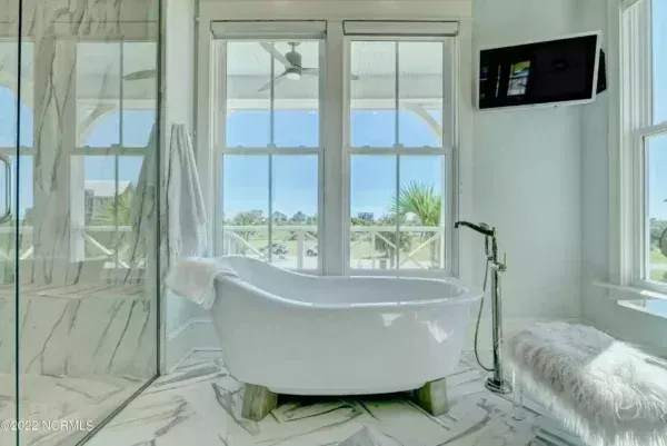 A bright, modern bathroom featuring a white freestanding soaking tub, marble flooring, and a large window with a view.