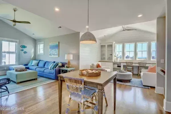 An open-plan living room with light hardwood floors, a blue sofa, a wooden dining table, and large windows.