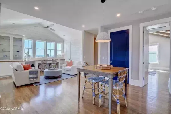 A bright, open-plan living and dining area with hardwood floors, a small dining table, chairs, and white armchairs.