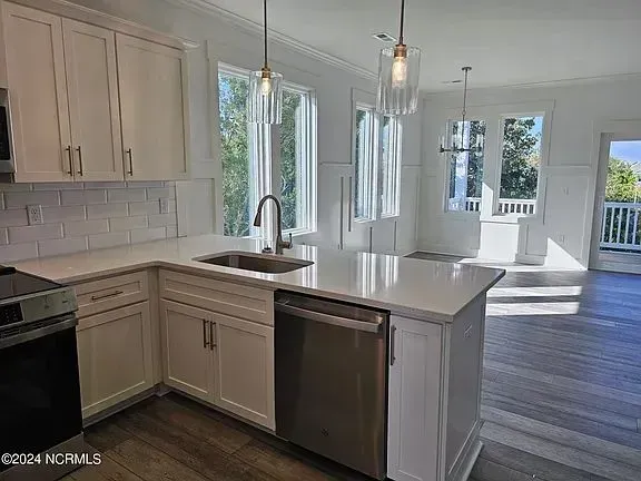 A modern kitchen with white cabinets, light countertops, a stainless steel dishwasher, and hanging pendant lights.