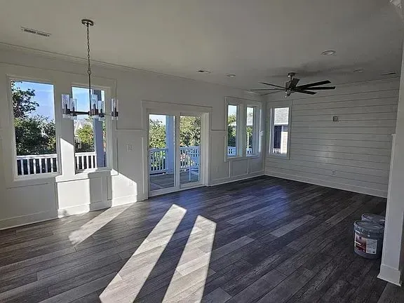 A bright, empty living area with wood-look floors, a shiplap wall, a ceiling fan, and sliding glass doors to a balcony.