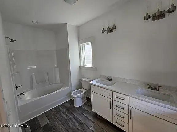 A bright modern bathroom with a white double vanity, dark wood-look flooring, and a shower-tub combo against the left wall.
