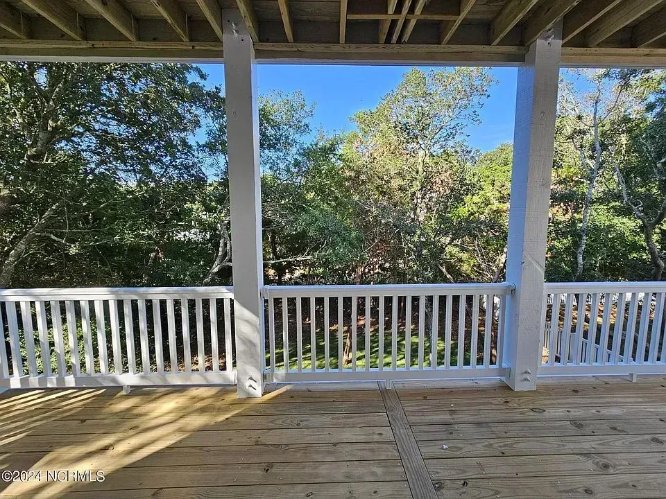 A wooden deck with a white railing overlooks a lush green wooded area under a clear blue sky.