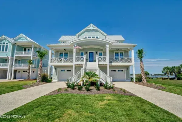A light green, two-story coastal home with white trim and a prominent front staircase, set under a clear blue sky.