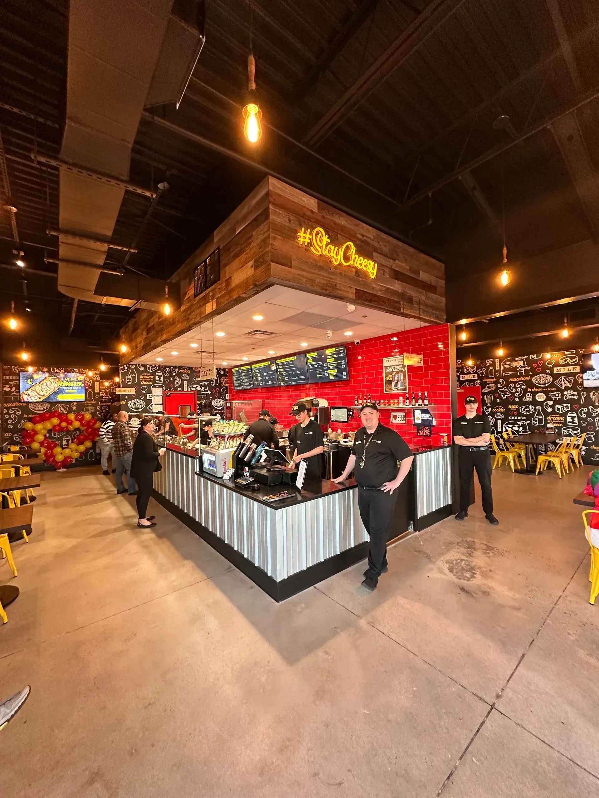 Employees stand behind the counter of a restaurant with rustic wood accents, red walls, and metal-paneled service desks.