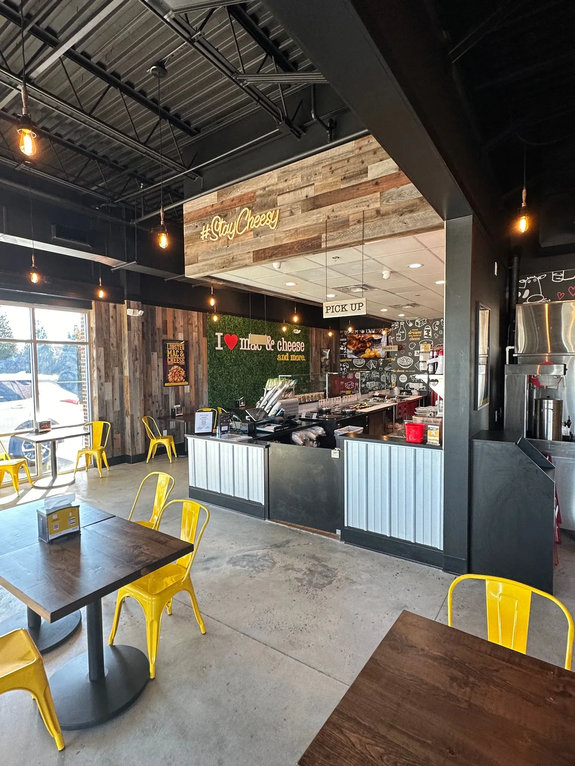 Interior of a restaurant with yellow chairs at wooden tables, a service counter, and a sign reading