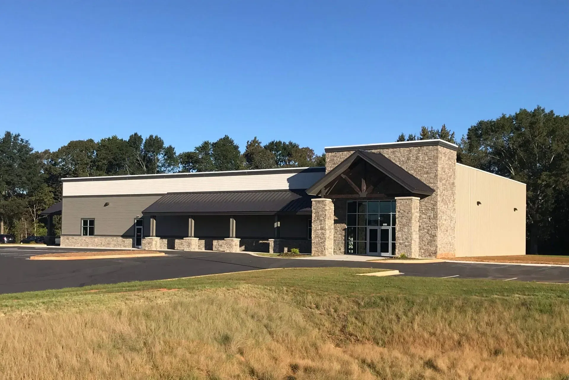 A one-story commercial building with stone accents, a dark metal entrance canopy, and a large paved parking lot.