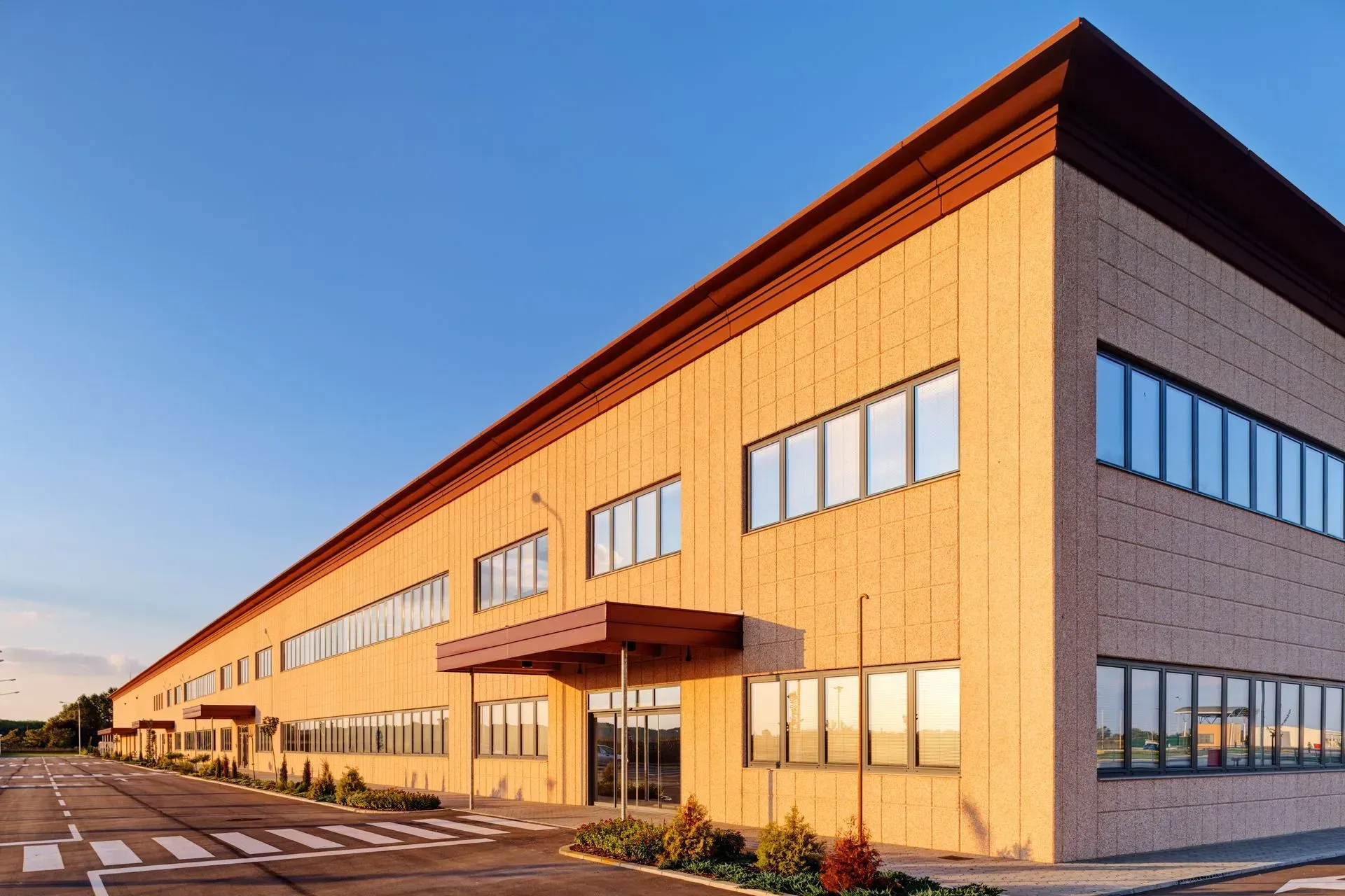 A long, multi-story commercial building with light brown brick walls and rows of windows under a clear blue sky.
