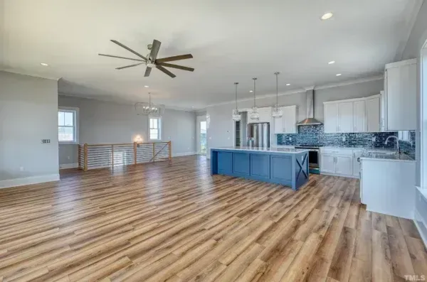 Open-concept kitchen and living area with wood-look flooring, a large blue island, and white cabinets.