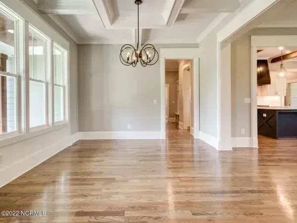 An empty dining room with light hardwood floors, neutral grey walls, a coffered ceiling, and a globe chandelier.