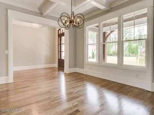 A dining area with light hardwood floors, neutral walls, a modern spherical chandelier, and large windows.