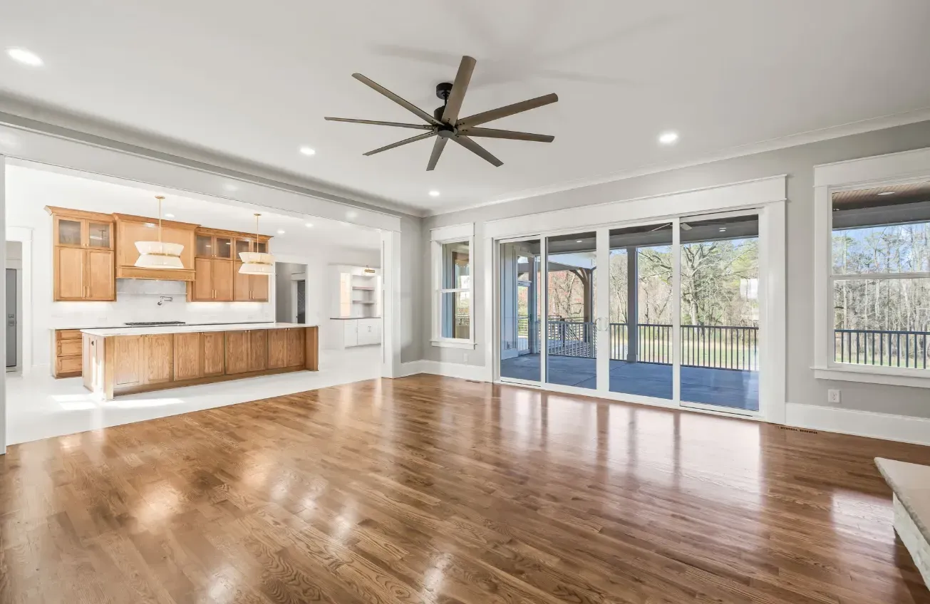 An open-concept living area with hardwood floors, a large ceiling fan, and a view of a patio through glass sliding doors.