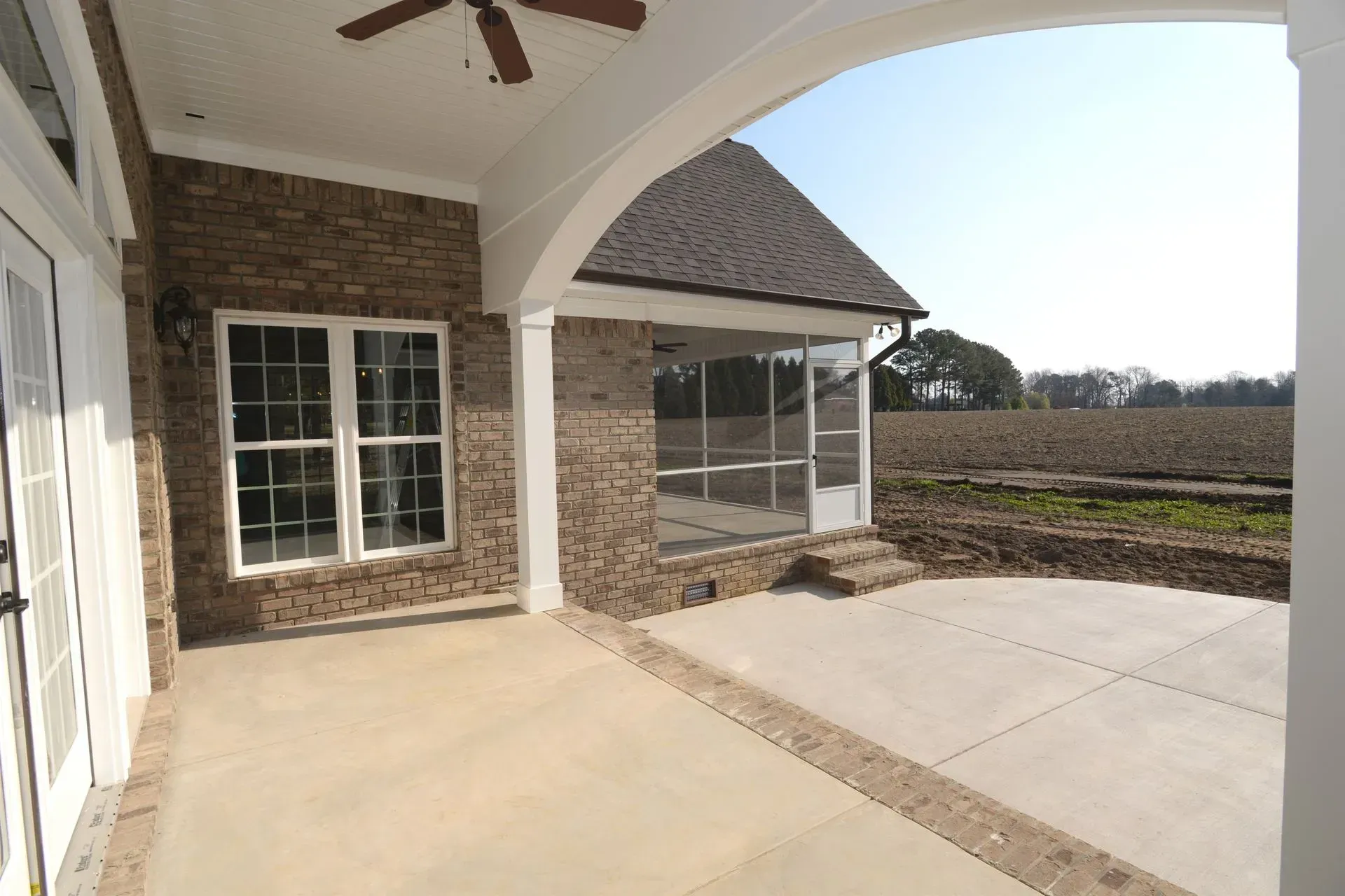 Covered patio with a brick exterior, a screened-in porch, and a concrete floor overlooking a field.