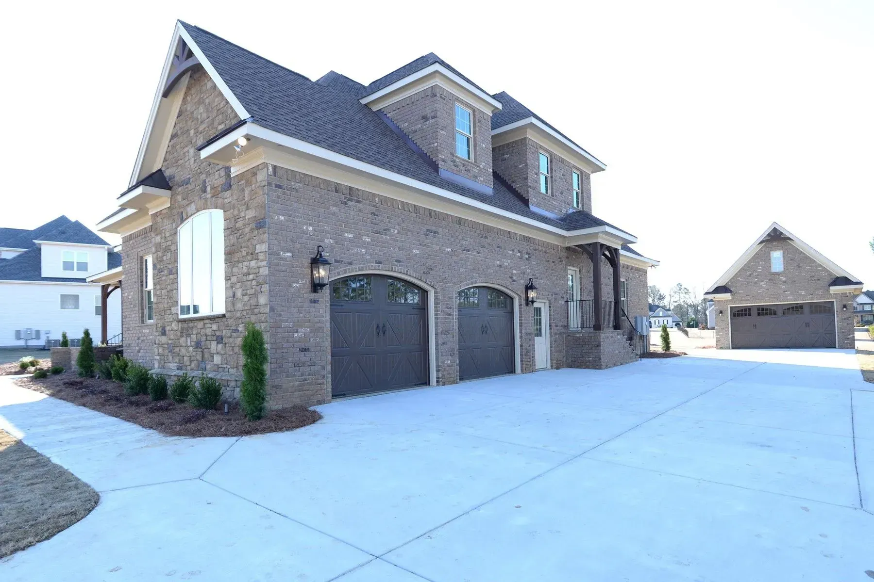 A tan brick two-story house with a three-car garage and a matching detached garage on a concrete driveway.