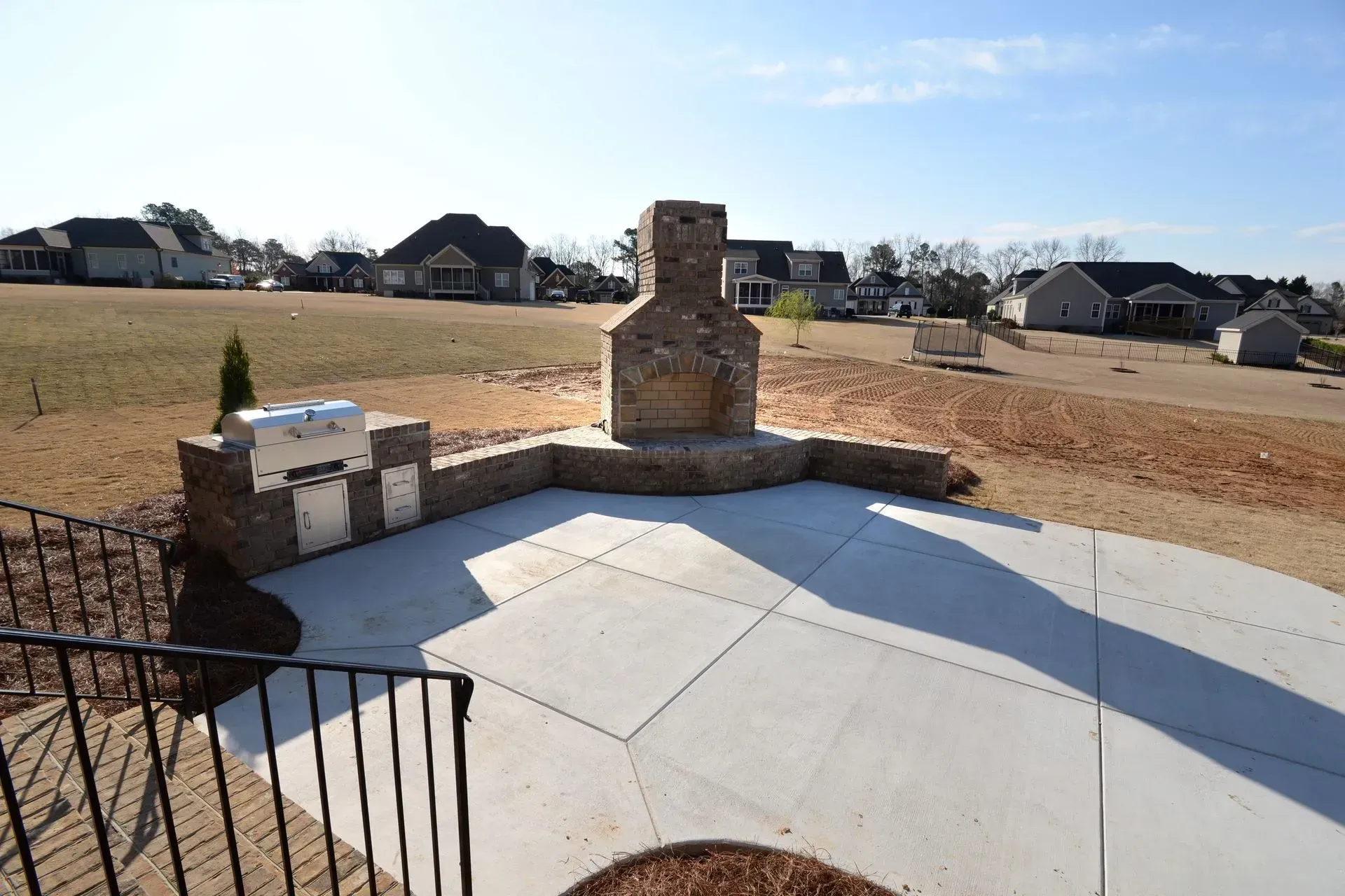 A stone fireplace and built-in grill on a concrete patio in a suburban backyard.