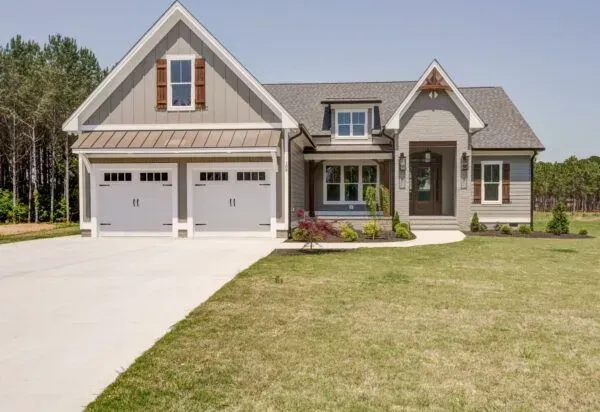 A two-story gray house with white trim, a two-car garage, a concrete driveway, and a lawn under a clear blue sky.