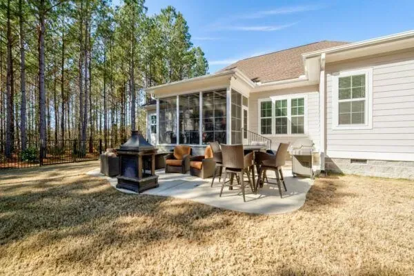 A back patio with a fire pit, patio furniture, and a screened-in porch, set against a backdrop of trees.