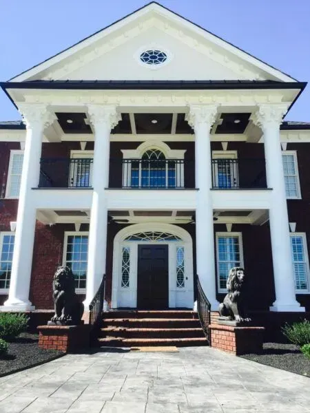 A brick two-story house with a white columned portico, a central front entrance, and two lion statues on the steps.