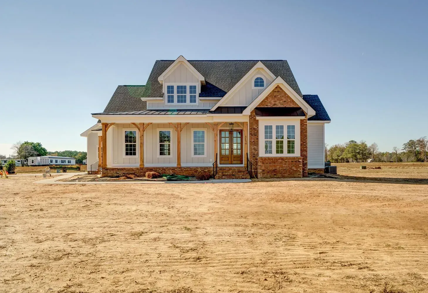 A newly constructed one-story farmhouse with white siding, brick accents, a dark roof, and a front porch.