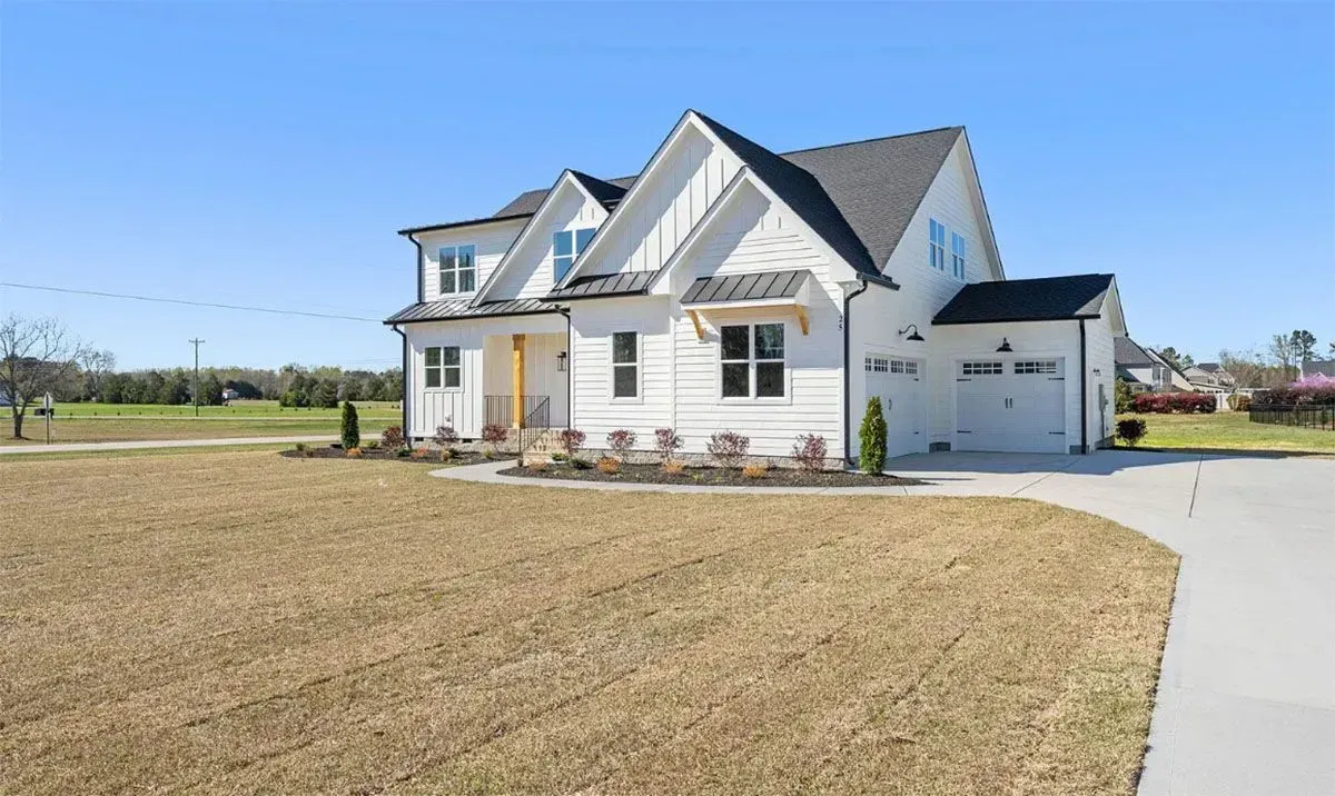 A white two-story modern farmhouse with a dark grey roof, dormer windows, and an attached two-car garage.