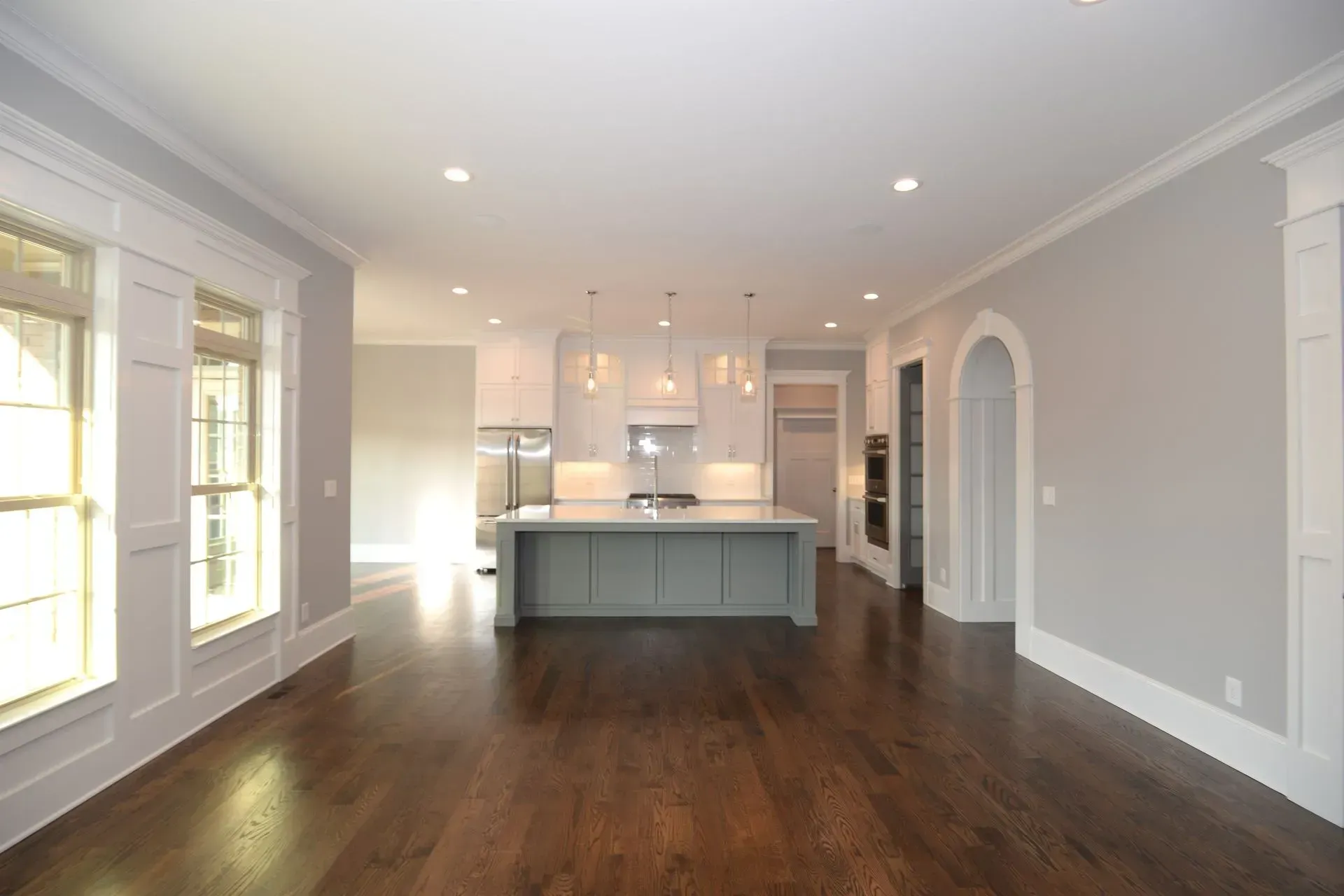 A spacious, light-filled kitchen with a gray island, dark wood floors, and white trim, viewed from an open dining area.