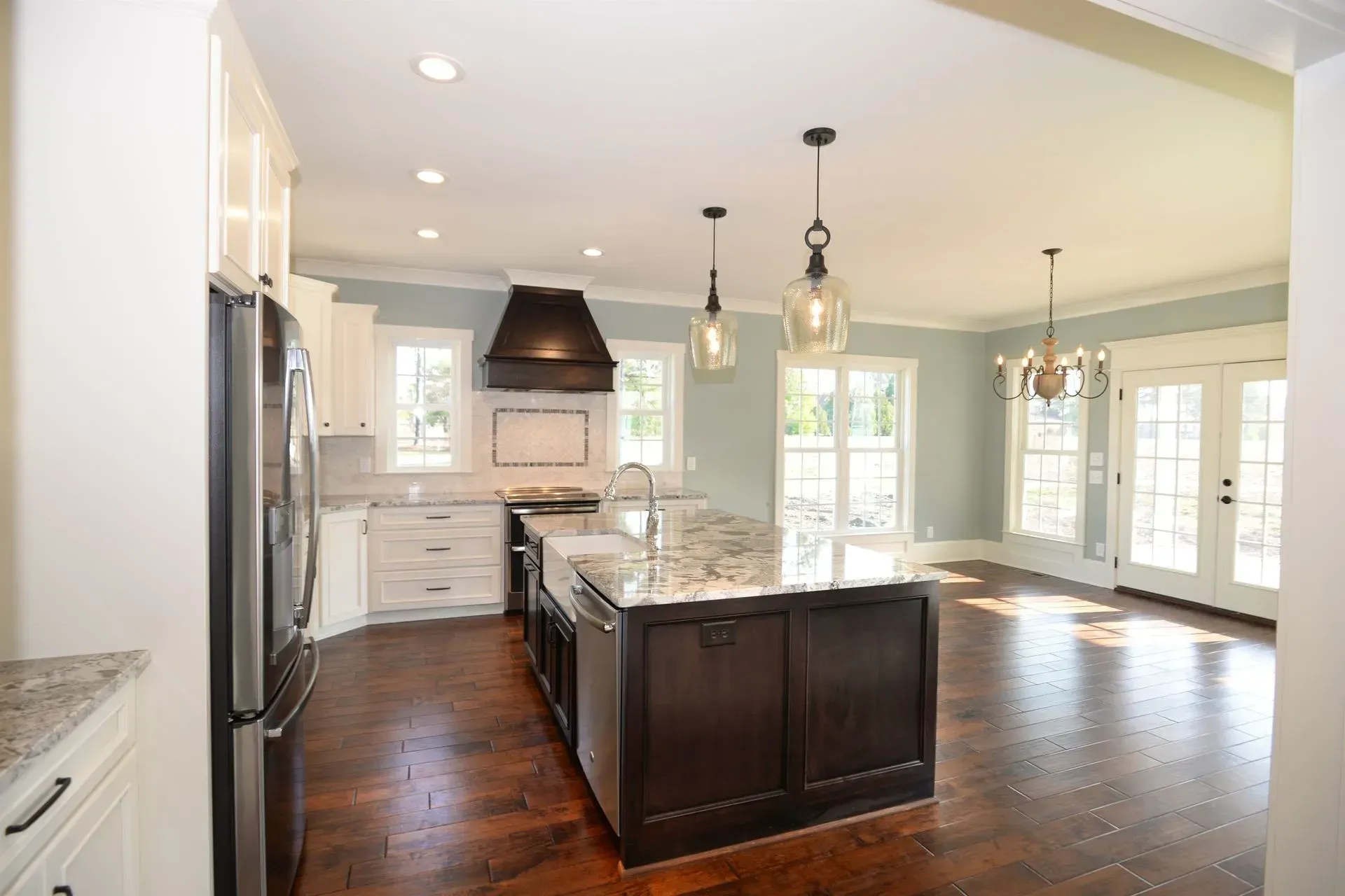 A kitchen with white cabinets, a dark wood island, a black range hood, and light blue walls over dark hardwood floors.