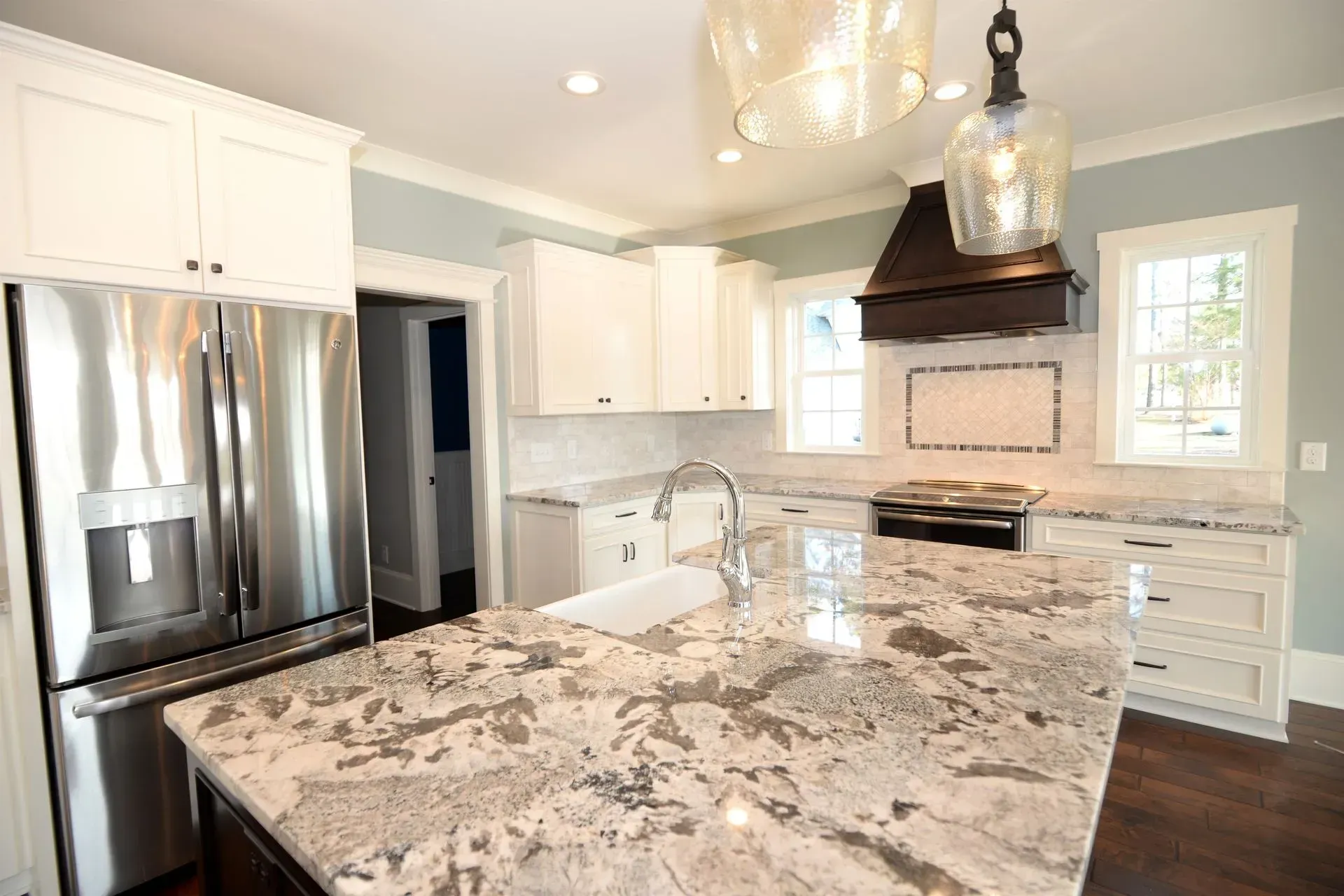 Modern kitchen featuring white cabinets, a large granite island, stainless steel appliances, and blue-gray walls.