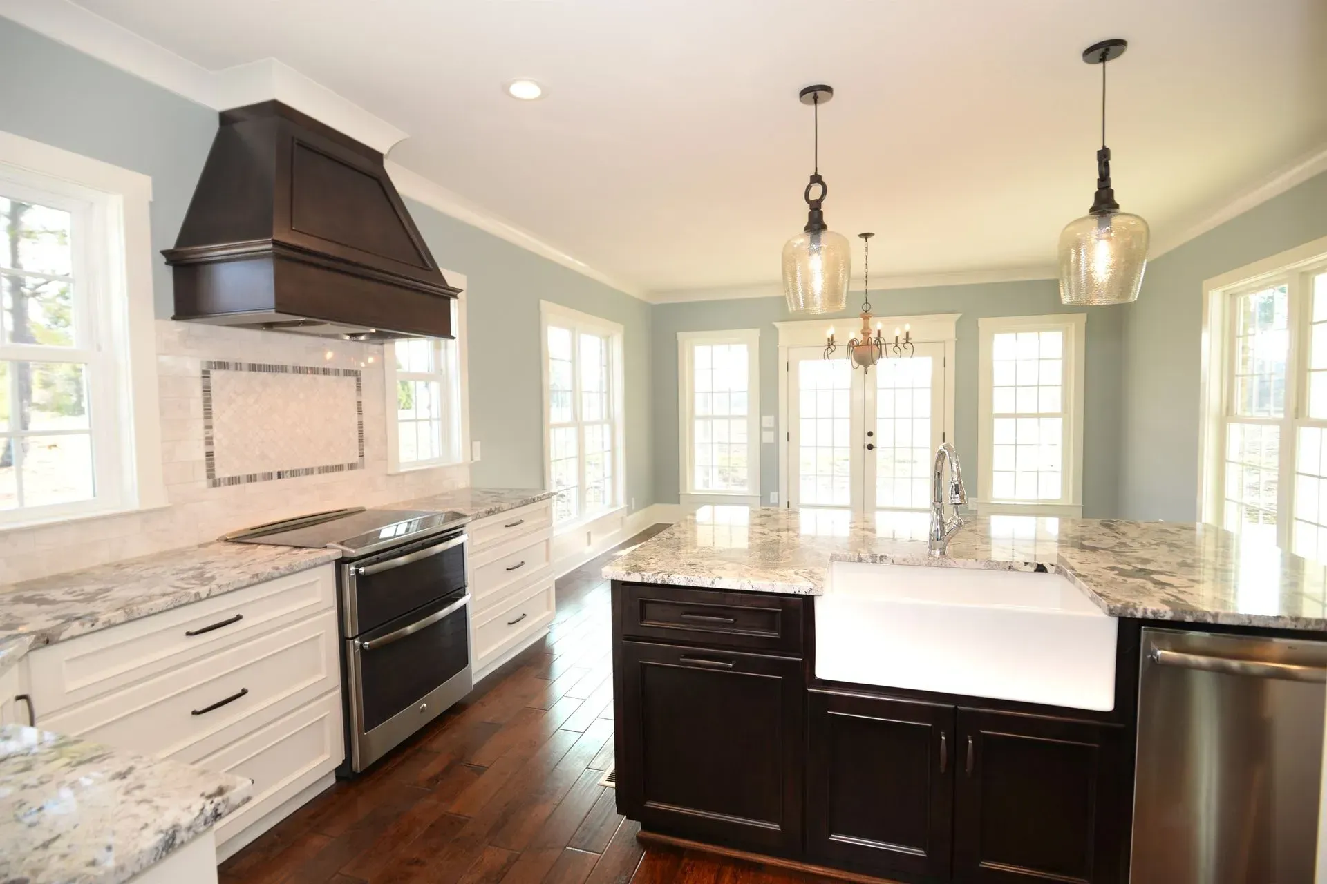 A modern kitchen with white cabinets, a dark wood island, a farmhouse sink, stainless appliances, and pale blue walls.