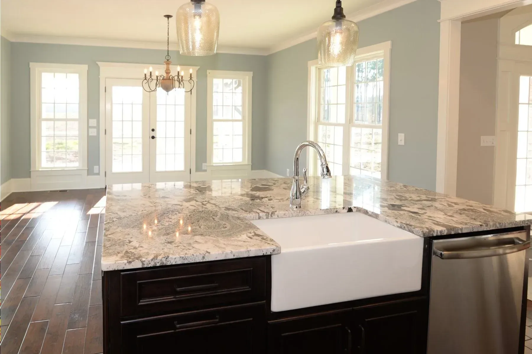 A modern kitchen island with a farmhouse sink, stone countertop, and dark cabinetry in a room with light blue walls.