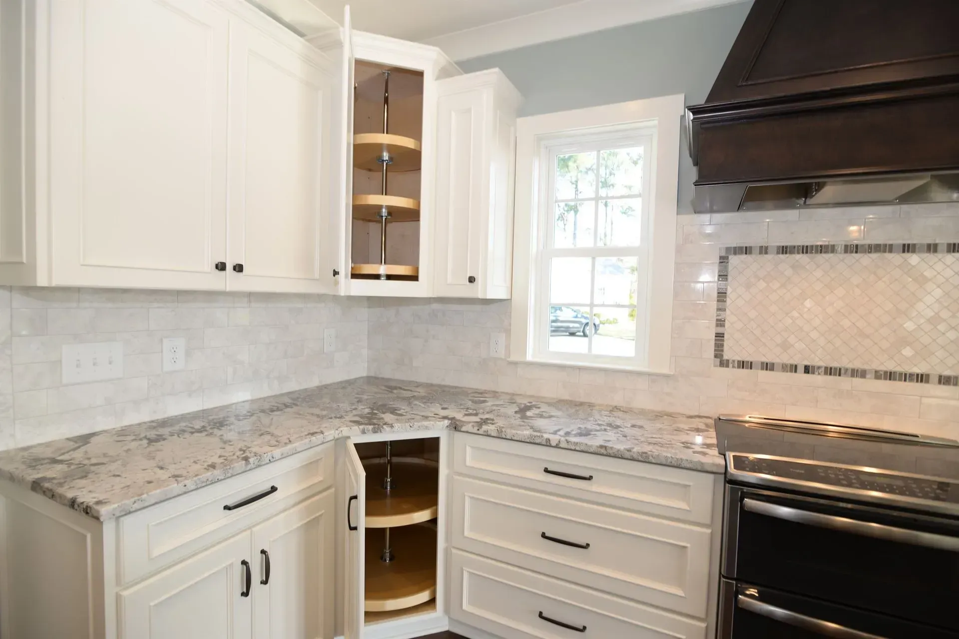 A kitchen corner featuring white cabinets, stone countertops, a tiled backsplash, and an open corner storage unit.