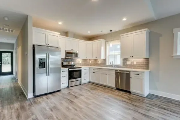 A modern kitchen with white cabinets, stainless steel appliances, and wood-look flooring.