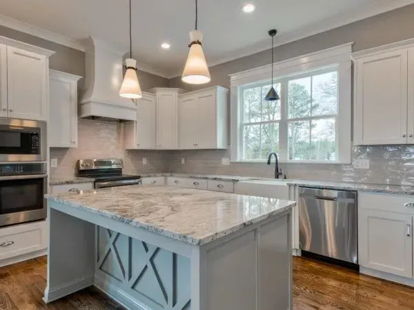 A bright kitchen with white cabinets, a central gray island, stainless steel appliances, and a window over the sink.