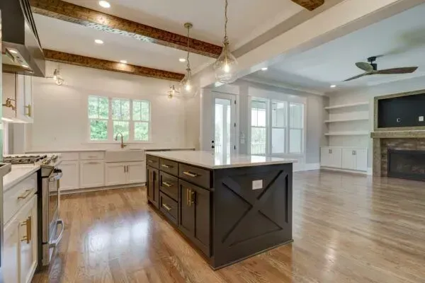 A kitchen with white cabinets, a large dark island with X-detailing, wood flooring, and exposed ceiling beams.